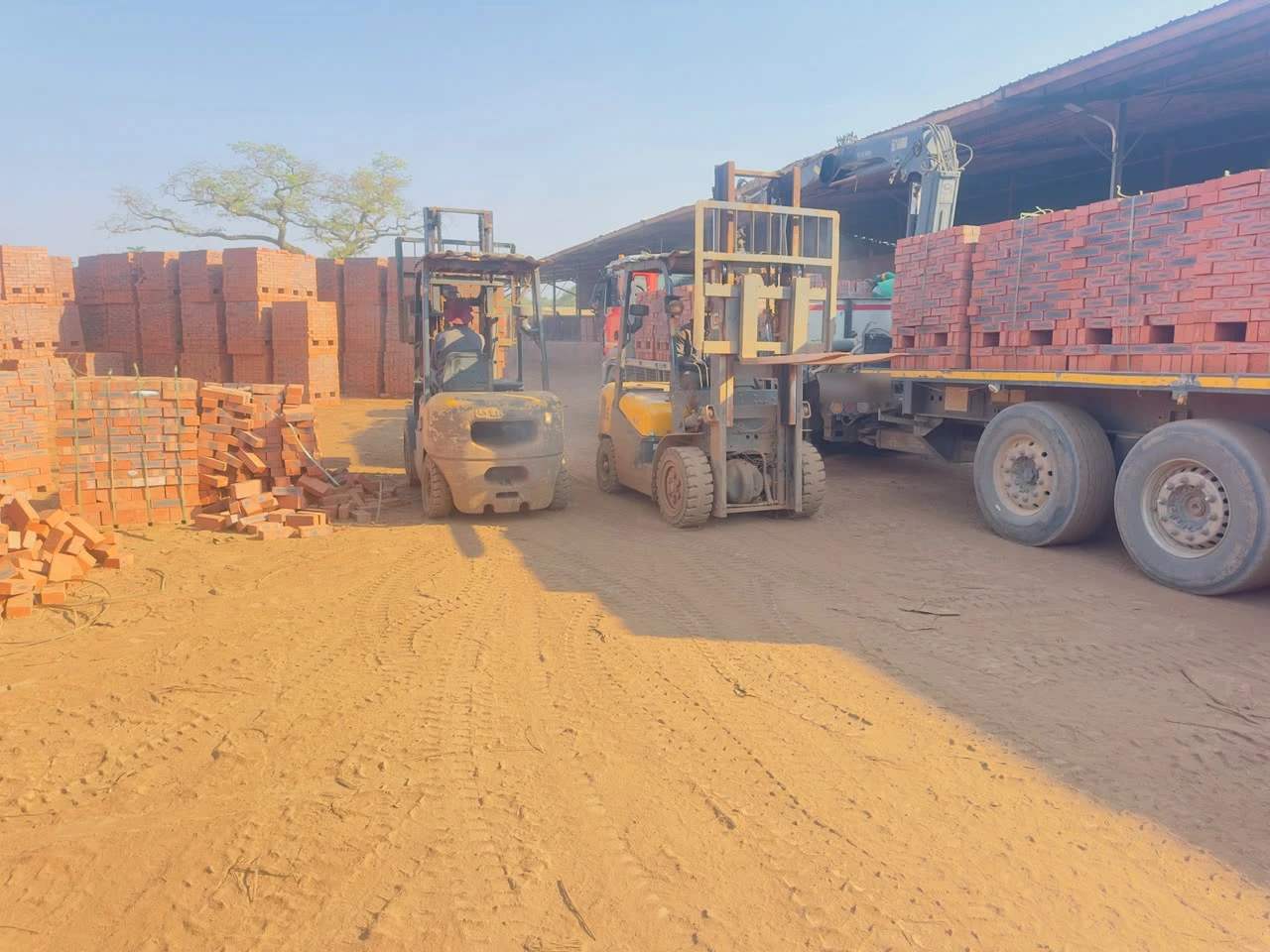 Two forklifts loading strapped pallets of face brick onto a crane truck at the AfroPacific brick site in Ruwa