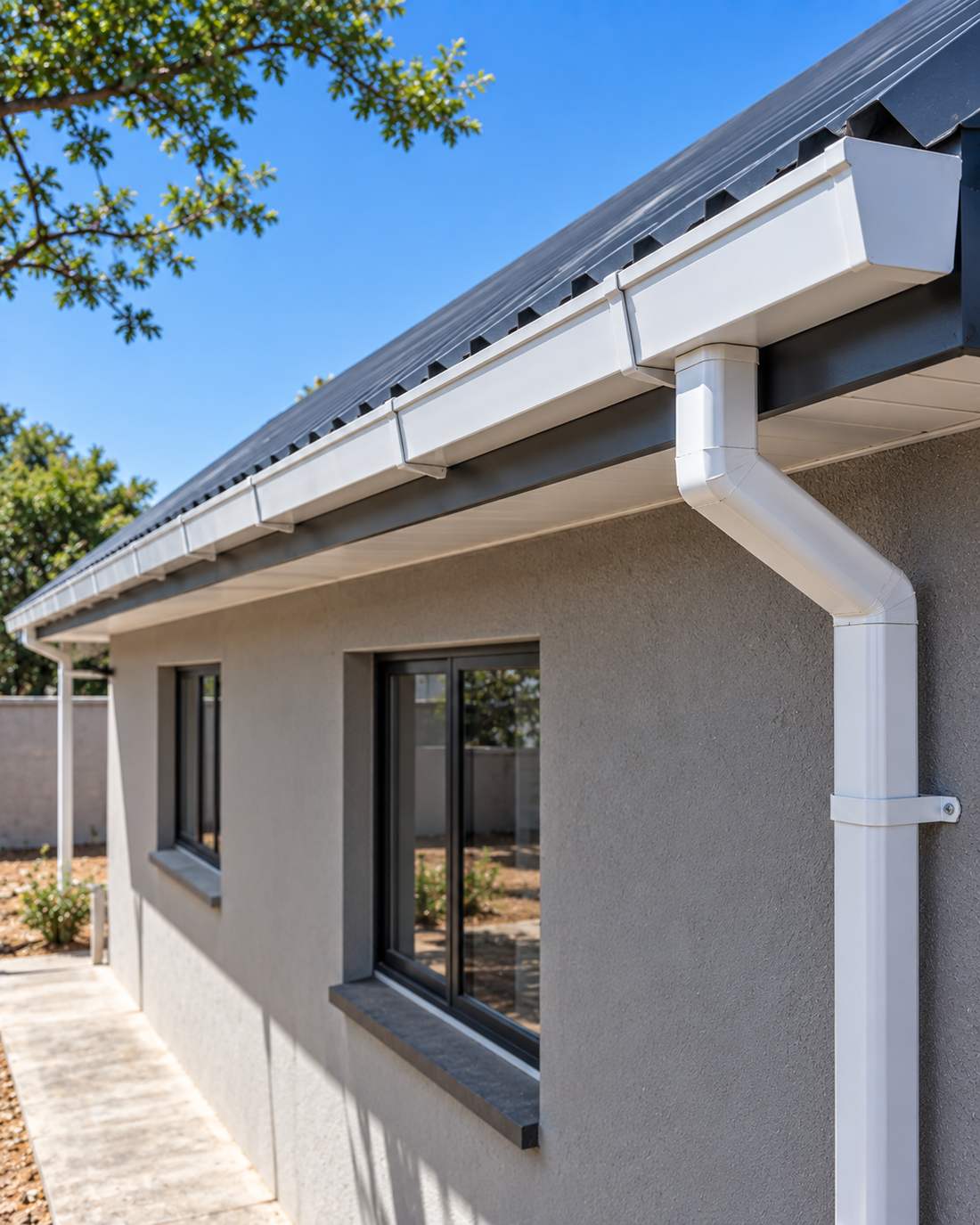 A white box gutter and downpipe newly fitted along the eaves of a charcoal roof